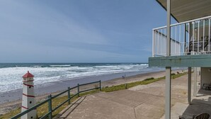 Een uitzicht op de kust met een vuurtoren, een betonnen voetpad en een overdekte zitplaats met uitzicht op het strand.