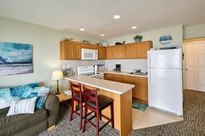 A compact kitchen with wooden cabinets, a white refrigerator, a microwave, and a coffee maker. There is a small dining area with a table and two chairs.