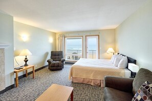 Quarto de hotel com cama, uma cadeira, uma mesa e vista para o mar através das portas da varanda.