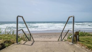 A concrete pathway leading to a beach with metal railings and ocean waves in the background. - King Suite - Top Floor - Ocean View - Beach Access - Pool & Hot Tub! (Lincoln City)