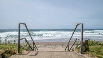 A concrete pathway leading to a beach with metal railings and ocean waves in the background.