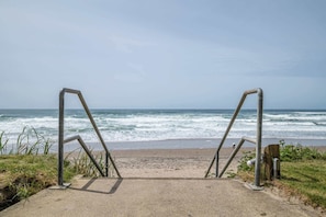 Een betonnen pad dat naar een strand leidt, met metalen leuningen en de oceaan op de achtergrond.