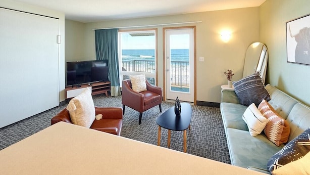 A hotel room with a bed, a television, a sofa, a chair, a small table, and a balcony with a view of the ocean. - King Suite - Top Floor - Ocean View - Beach Access - Pool & Hot Tub! (Lincoln City)