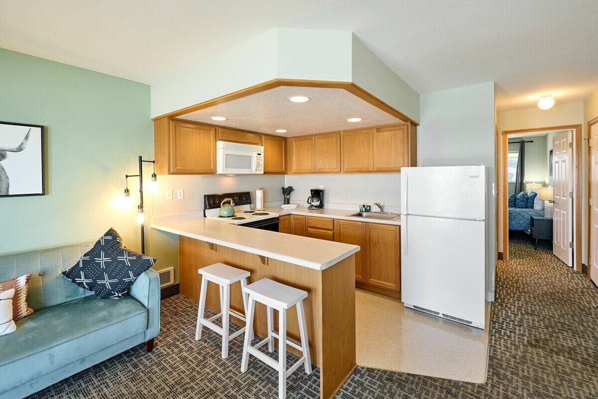 A compact kitchen with wooden cabinets, a microwave, a refrigerator, and a bar stool.