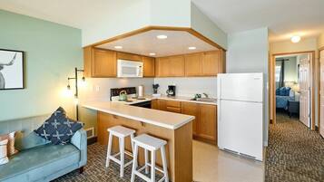 A compact kitchen with wooden cabinets, a microwave, a refrigerator, and a bar stool.