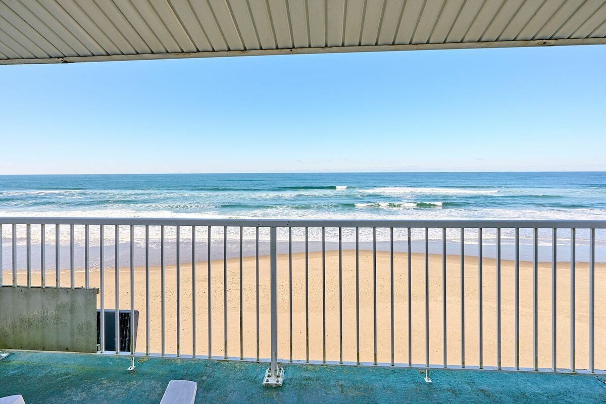 A beach view from a balcony with a railing, a concrete structure, and a clear sky.