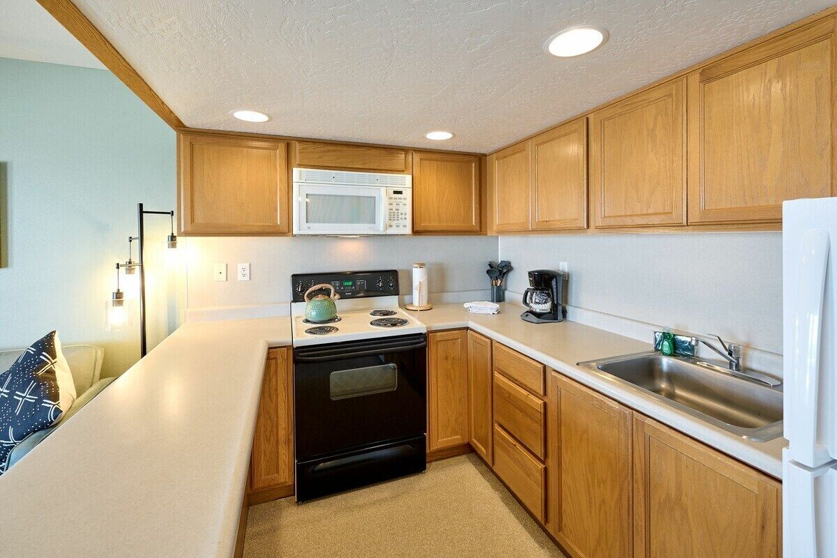 A compact kitchen with wooden cabinets, a microwave, a stove, and a sink.