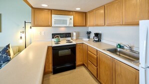 A compact kitchen with wooden cabinets, a microwave, a stove, and a sink. - King Suite - Top Floor - Ocean View - Beach Access - Pool & Hot Tub! (Lincoln City)