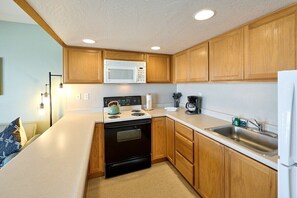 A compact kitchen with wooden cabinets, a microwave, a stove, and a sink.
