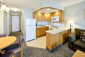 A compact kitchen with wooden cabinets, a microwave, a refrigerator, and a dining area with a table and chairs.