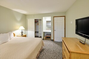 A hotel room with a bed, a TV, a desk, a lamp, and a closet with a window.
