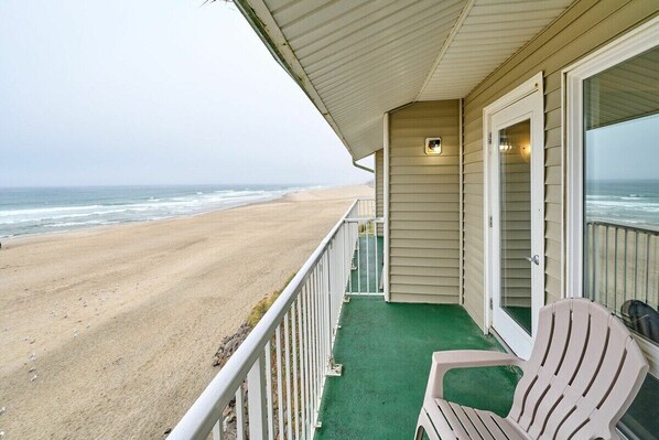 A beachside balcony with a view of the ocean, a chair, and a door leading to the interior.