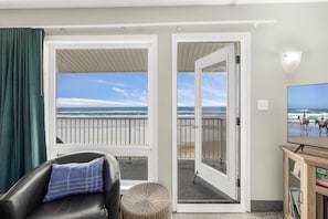 Quarto com vista para a praia, varanda, poltrona de couro, banquinho de vime e televisão.