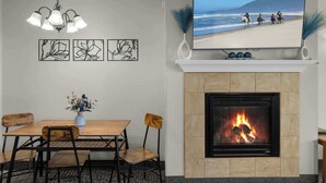 A dining area with a fireplace, a TV mounted above it, and a coastal view on the screen. - Top Floor Ocean View Suite - Sleeps Six - Pool & Hot Tub Access! (Lincoln City)