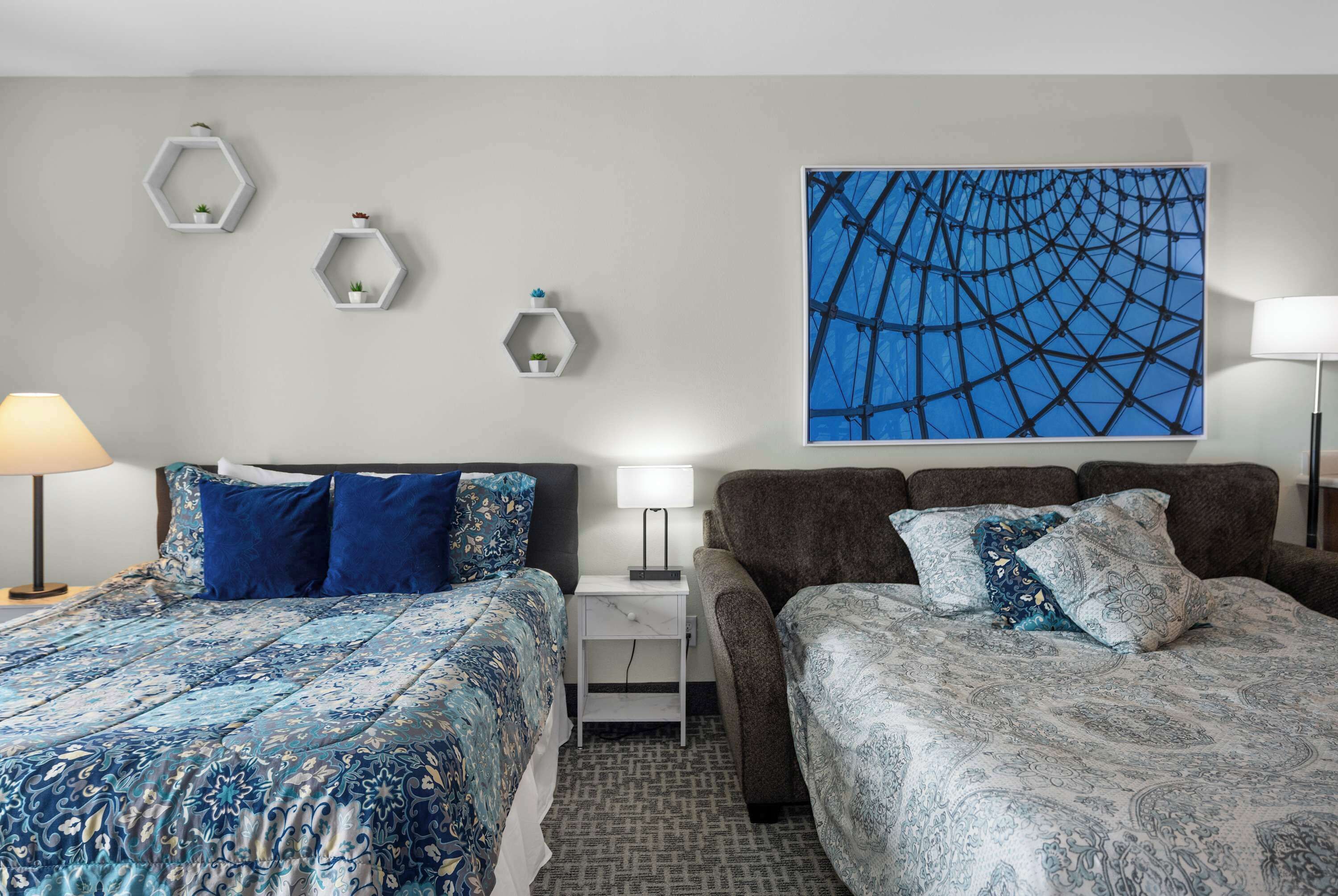 Een hotelkamer met twee bedden, een nachtkastje, een lamp en een groot abstract schilderij aan de muur.