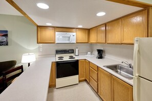 A compact kitchen with wooden cabinets, a microwave, stove, sink, and a refrigerator. - Oceanfront Family Suite With Full Kitchen, Beach Access, Pool & Hot Tub (Lincoln City)