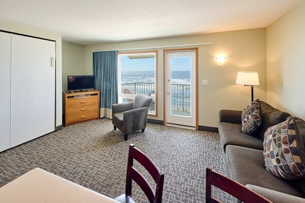 A hotel room with a balcony, a sofa, a TV, a desk, and a lamp.
