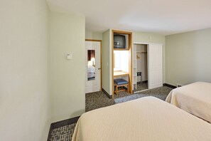 A hotel room with two beds, a desk with a television, a wardrobe, and a bathroom visible through an open door.