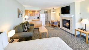 Habitación de hotel con cama, sofá, mesa de comedor, chimenea y una zona de cocina al fondo.