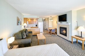 Een hotelkamer met een bed, een bank, een eettafel, een open haard en een keuken op de achtergrond.