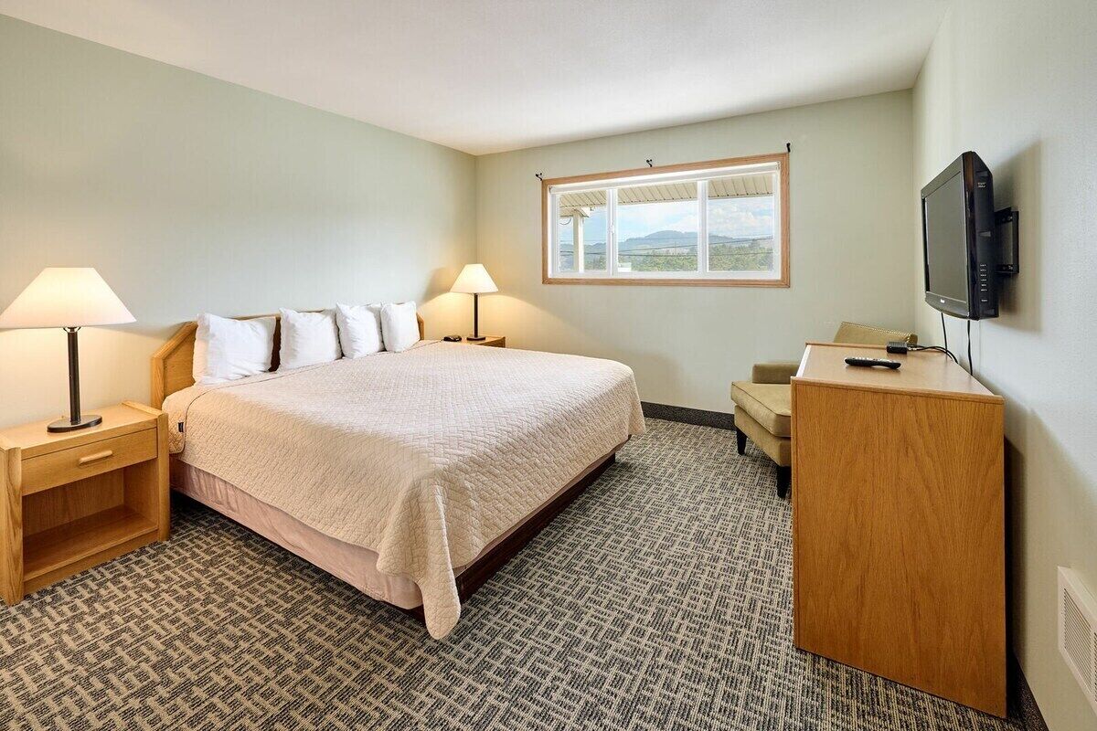 A hotel room with a bed, two bedside tables with lamps, a desk with a television, and a window with a view.