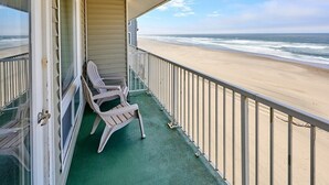 Un balcón con vista a la playa, una silla y una barandilla.