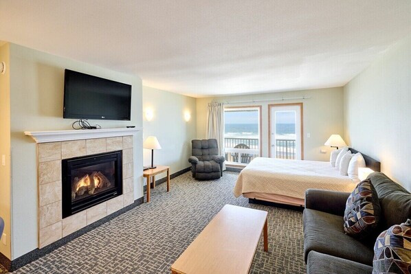 A hotel room with a fireplace, a bed, a sofa, a television, and a view of the ocean.