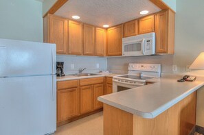 A kitchen with wooden cabinets, a white refrigerator, a microwave, and a stove. - Stunning Oceanfront Suite - Sleeps Six - Top Floor - Heated Pool & Hot Tub Access! (Lincoln City)