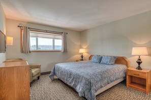 A hotel room with a bed, bedside lamps, a desk, a chair, and a window with curtains.