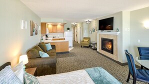 A hotel room with a bed, a sofa, a dining table, a fireplace, a TV, and a kitchenette. - Deluxe Ocean View Family Suite - Sleeps Six - Heated Pool & Hot Tub! (Lincoln City)
