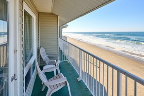 A beachfront property with a balcony, white plastic chairs, and a view of the ocean.