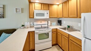 A compact kitchen with wooden cabinets, a microwave, a stove, and a refrigerator. - Deluxe Ocean View Family Suite - Sleeps Six - Heated Pool & Hot Tub! (Lincoln City)