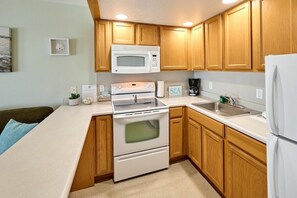 A compact kitchen with wooden cabinets, a microwave, a stove, and a refrigerator.