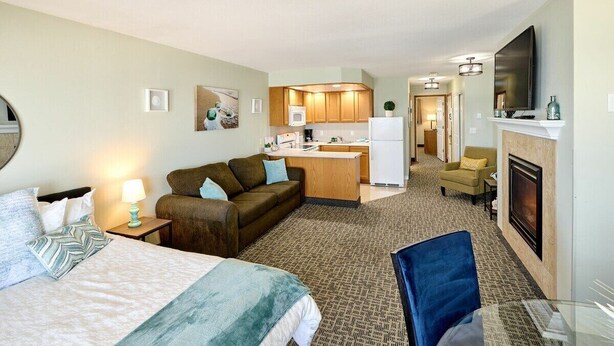 A hotel room with a bed, a sofa, a small kitchenette, a TV, and a fireplace. - Deluxe Ocean View Family Suite - Sleeps Six - Heated Pool & Hot Tub! (Lincoln City)
