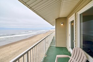 Ein Balkon mit Blick auf den Strand, ein Stuhl und eine Tür mit einem Fenster.