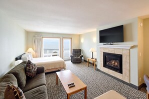 Une chambre d’hôtel équipée d’un lit, d’un canapé, d’un fauteuil, d’une cheminée, d’une télévision et offrant une vue sur la mer par la fenêtre.