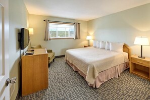 A hotel room with a bed, bedside tables, a desk, a television, and a window with curtains.