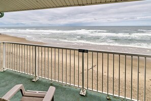 Uitzicht op het strand vanaf een overdekt balkon met een metalen hekwerk, een bankje en een bordje met de tekst 'zwemmen verboden'.