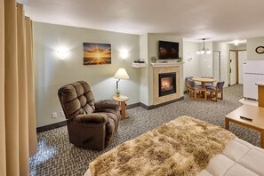 Een woonkamer met een open haard, een televisie erboven en een eethoek met een tafel en stoelen.
