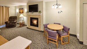 A hotel room with a fireplace, a television mounted above it, a dining table with chairs, a sofa, and a lamp. - Stunning Top Floor Corner Suite for 6! Beautiful Ocean Views & Easy Beach Access! (Lincoln City)
