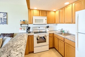 A kitchen with wooden cabinets, a white microwave, a stove, and a sink. - Amazing Ocean View Suite - Sleeps Six - Pool Access & Hot Tub! (Lincoln City)