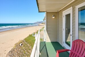 A beachfront property with a balcony overlooking the ocean, a red chair, and a door leading to a covered area.