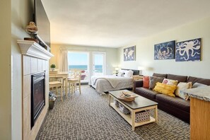 A hotel room with a bed, a sofa, a desk, and a fireplace. There is a view of the ocean through the windows. - Amazing Ocean View Suite - Sleeps Six - Pool Access & Hot Tub! (Lincoln City)