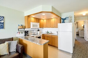 A compact kitchen with wooden cabinets, a white refrigerator, and a built-in microwave. - Amazing Ocean View Suite - Sleeps Six - Pool Access & Hot Tub! (Lincoln City)
