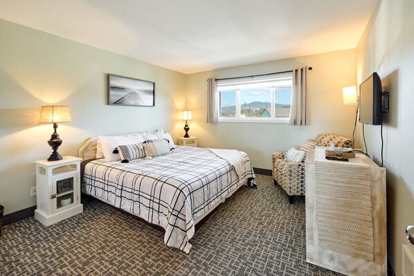 A hotel room with a bed, bedside tables, a TV, a window with curtains, and a view of the outside.