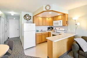 A compact kitchen with wooden cabinets, a white refrigerator, a microwave, a stove, and a small island counter.
