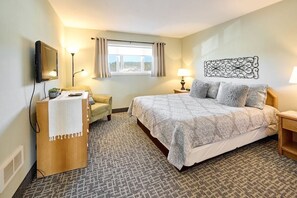 A hotel room with a bed, a desk with a lamp, a chair, a TV, and a window with curtains. - Ocean View Suite - Sleeps Six - Heated Indoor Pool & Hot Tub Access (Lincoln City)