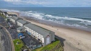 A coastal motel with a parking lot, a beach view, and a building with a red door. - Ocean View Suite - Sleeps Six - Heated Indoor Pool & Hot Tub Access (Lincoln City)
