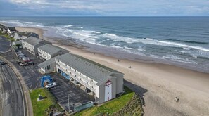 A coastal motel with a parking lot, a beach view, and a building with a red door. - Ocean View Suite - Sleeps Six - Heated Indoor Pool & Hot Tub Access (Lincoln City)