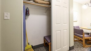 A room with a closet, a broom, a chair, and a table.